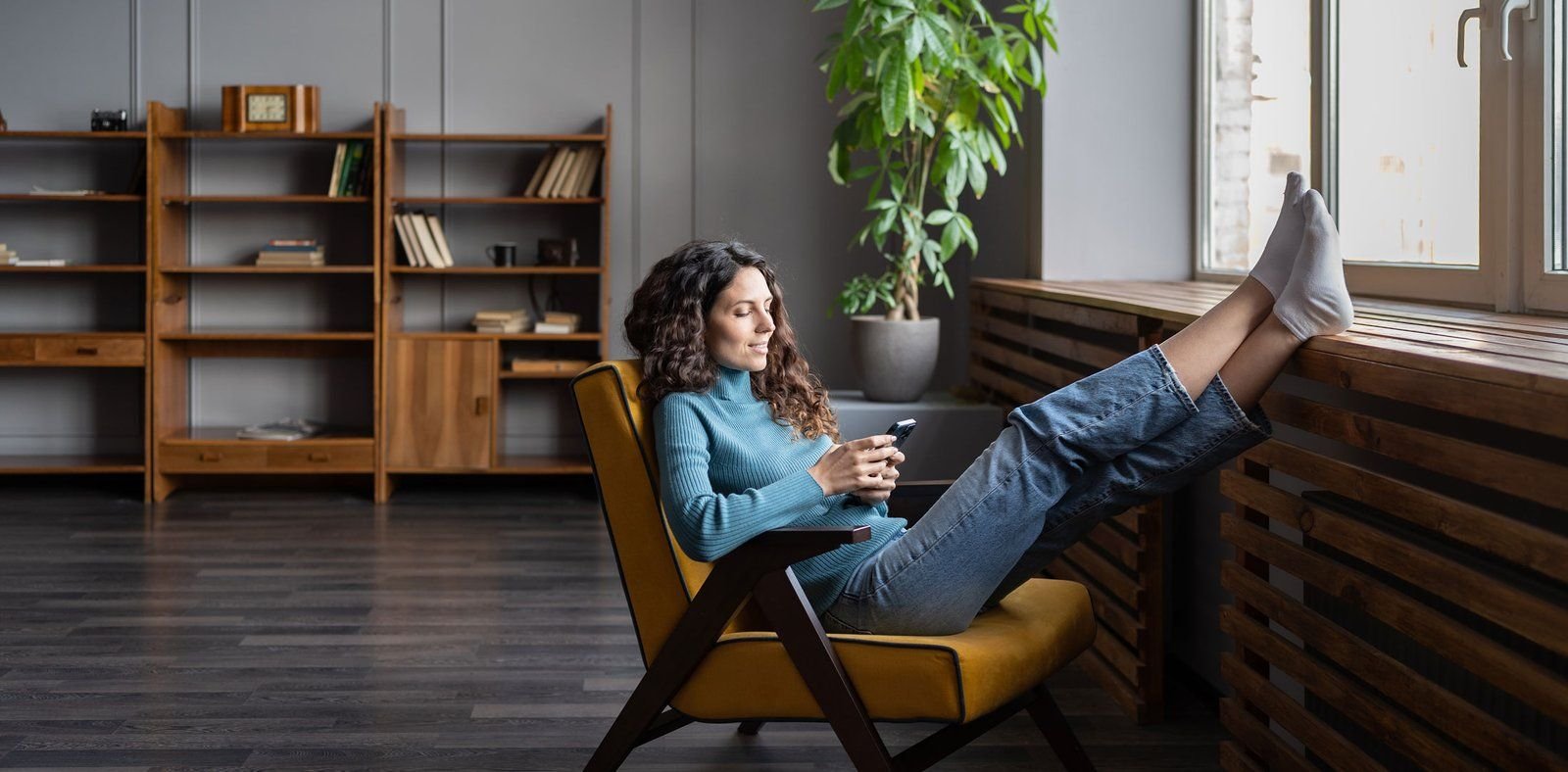 A woman sitting in an armchair with her feet up, looking at her phone