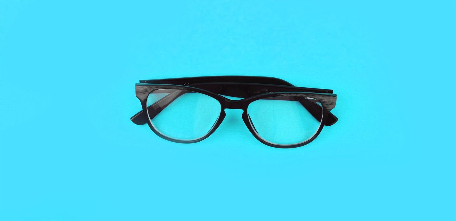 A pair of black-framed glasses on a turquoise background
